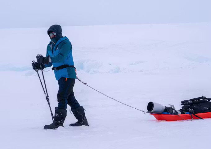Photographer with sled and hiking poles in Antarctica, heading to an emperor penguin colony