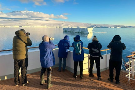 A group of Antarctic tourists stand on the deck of MS Adventurer in the Ross Sea photographing a tabular iceberg
