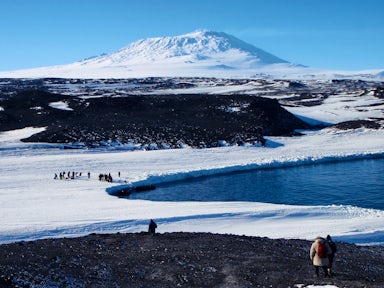 A group of tourists on the ice on Ross Island, with snow and black volcanic sand and Mount Erebus on the horizin