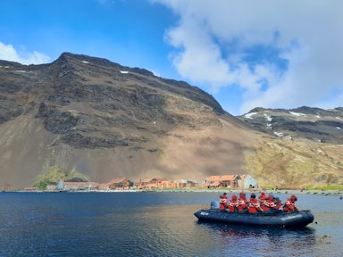 Expedition cruise passengers zodiac cruising  past the abandoned and rusting remains of the whaling station at Stromness harbour, South Georgia