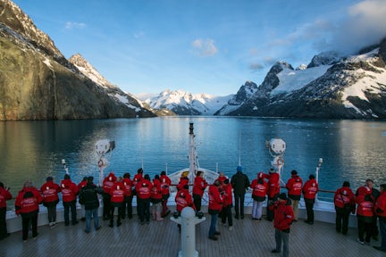 Passengers looking over the bow of an expedition cruise ship looking at the glaciers and mountains at the head of Dryglaski Fjord, South Georgia
