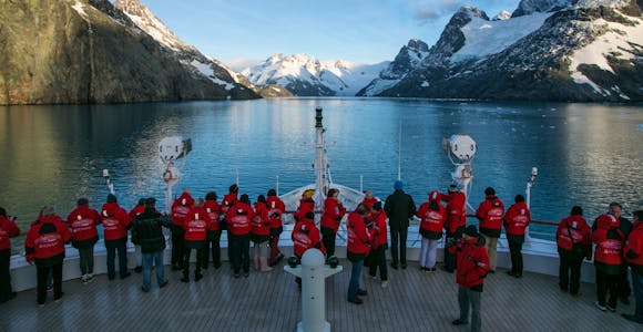 Passengers looking over the bow of an expedition cruise ship looking at the glaciers and mountains at the head of Dryglaski Fjord, South Georgia