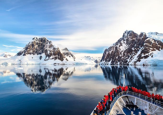 The bow of a ship is shown sailing through the glassy sea of the Lemaire Channel