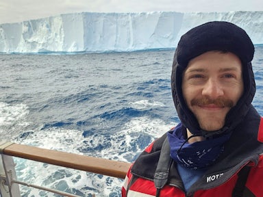 Colin, a Swoop sales team member, takes a selfie in front of an iceberg while out on the deck of an Antarctic ship 