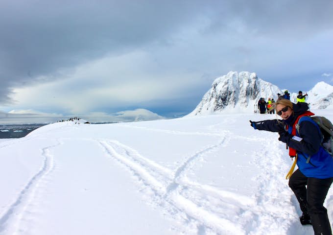 A woman points excitedly to a group of penguins in the background in Antarctica