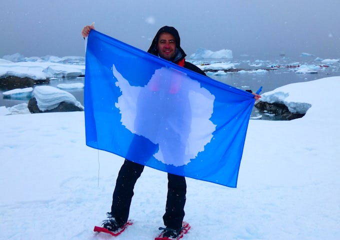 A man holds up an Antarctic flag while on the 7th Continent 