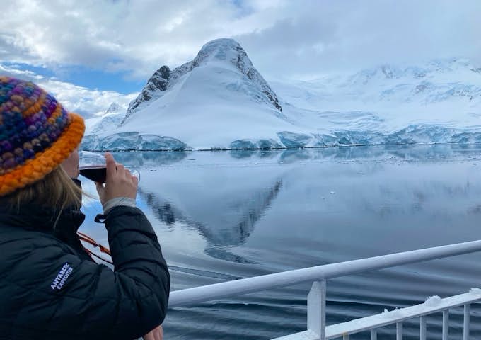 A woman drinks red wine while looking out onto a view of Antarctica 