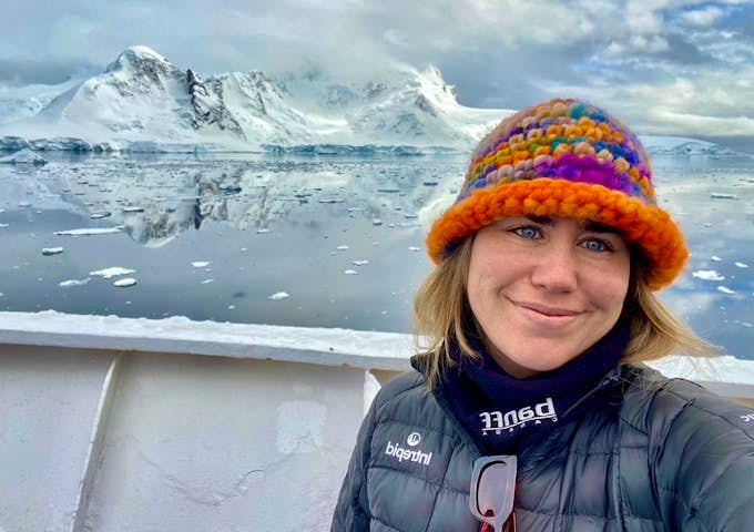 A woman wears a colourful hat while taking a selfie in Antarctica