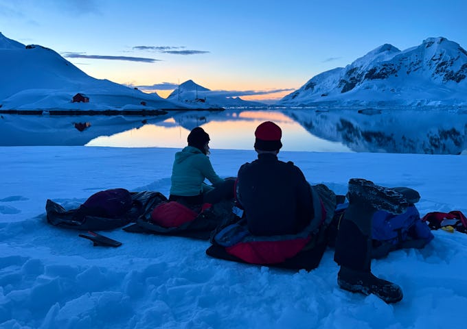 Two people enjoy the sunset while camping on Antarctica 