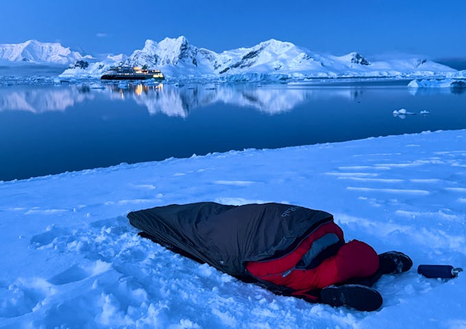 A sleeping bag lies on the ground in front of an Antarctic bay at dusk 