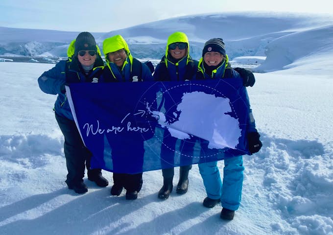 Four toursits in the snow hold an Antarctic flag to celebrate reaching the 7th Continent