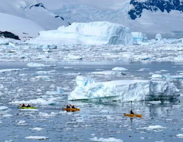 Three kayaks paddle among the ice in Antarctica
