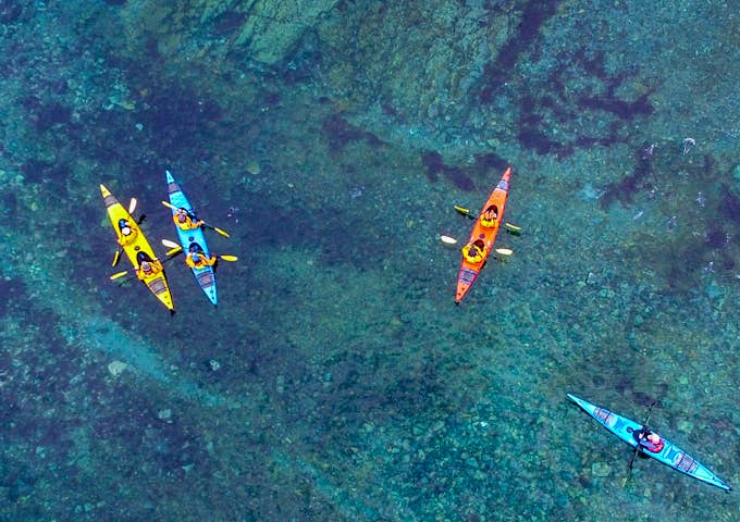A drone shot of four kayakers in deep greeny-blue Antarctic water