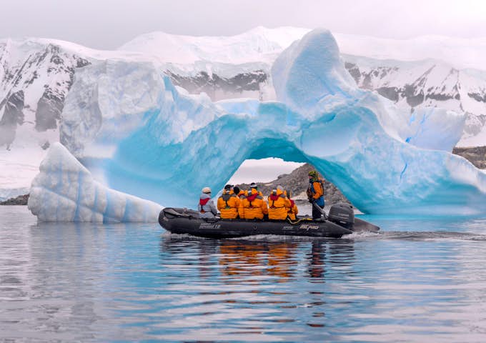 A zodiac cruises in front of an ice arch in Cuverville