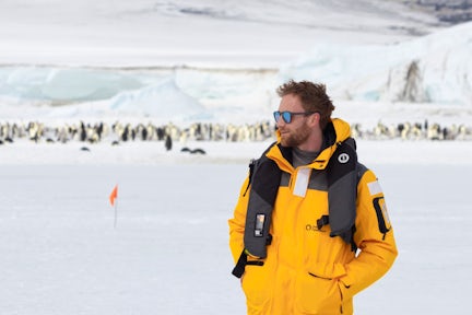 A man stands in front of the emperor penguins of Snow Hill, Antarctica